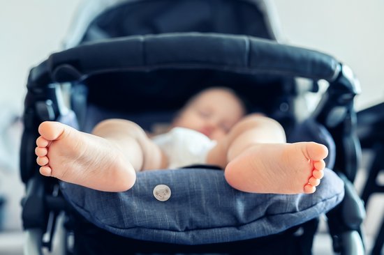 Slapende baby in een kinderwagen met een Squitos sticker op de stof bij de voeten.