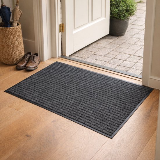 Donkergrijze ribbel deurmat met antislip rand, bij een open deur met schoenen ernaast.