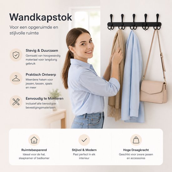 Vrouw met een blauwe blouse en spijkerbroek hangt een sjaal en jas aan een zwarte wandkapstok.