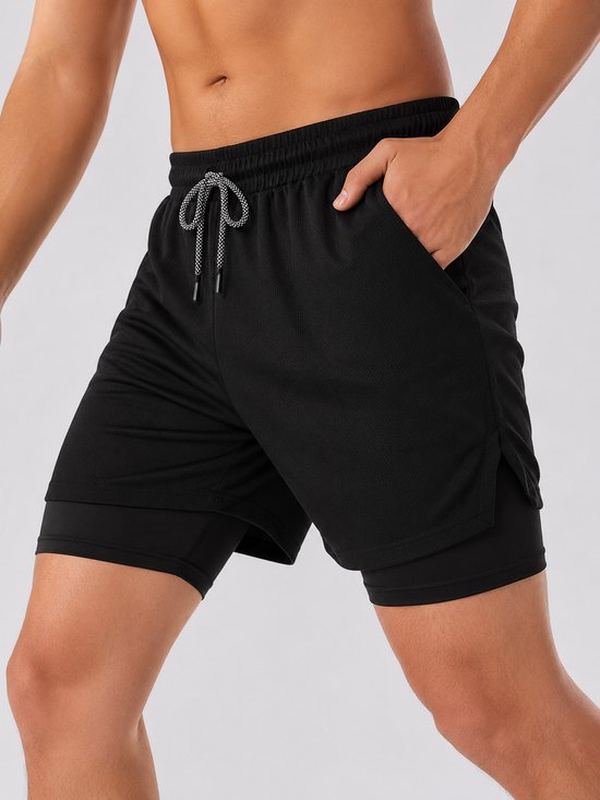 Homme en short de sport noir, avec la main dans une poche. Vue détaillée du short à double couche.