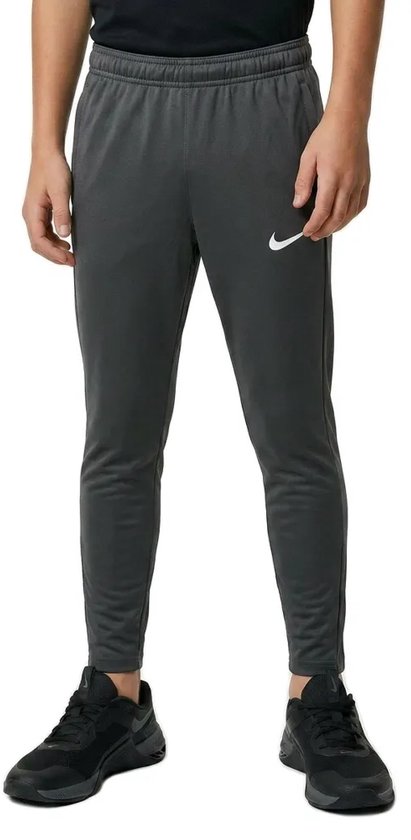 Jongen in een donkergrijze Nike trainingsbroek met witte swoosh op de linkerpijp.