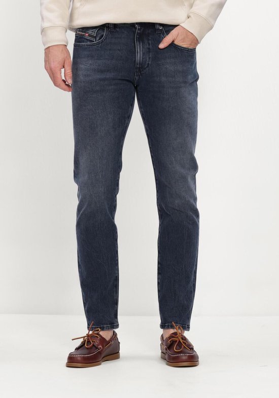 Man draagt een donkerblauwe jeans met een lichtbeige hoodie en bruine instappers.