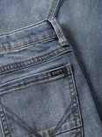 Close-up van de achterzak van een spijkerbroek met een klein zwart label met "ORG.DENIM PRODUCTS BY NAME IT" erop.