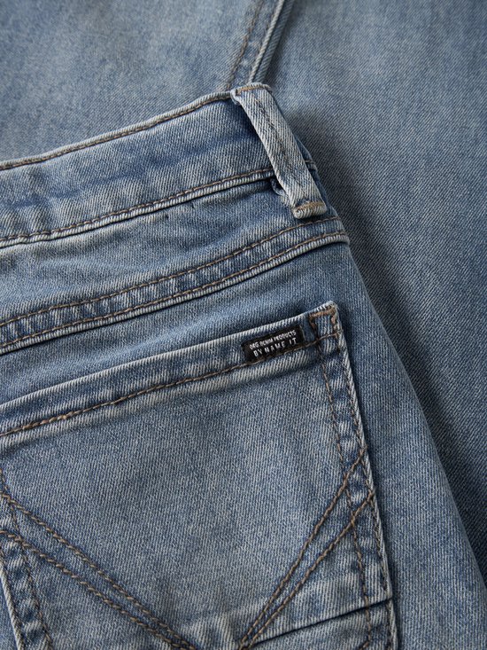 Close-up van de achterzak van een spijkerbroek met een klein zwart label met "ORG.DENIM PRODUCTS BY NAME IT" erop.