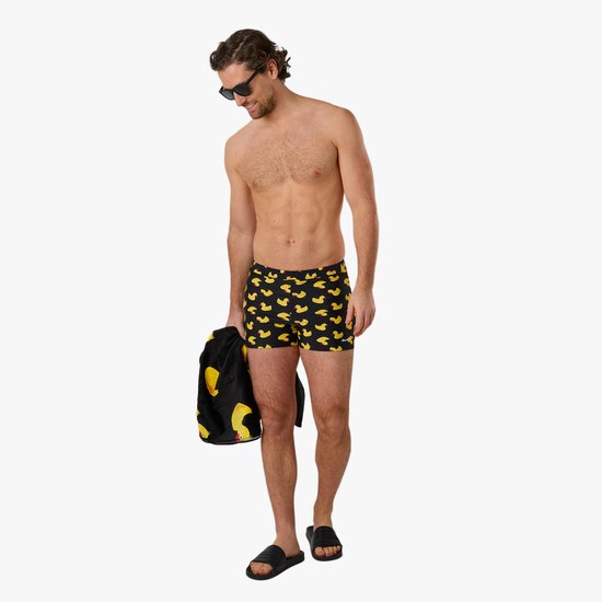 Man met zwembroek met badeendjesprint en handdoek, lachend naar beneden kijkend