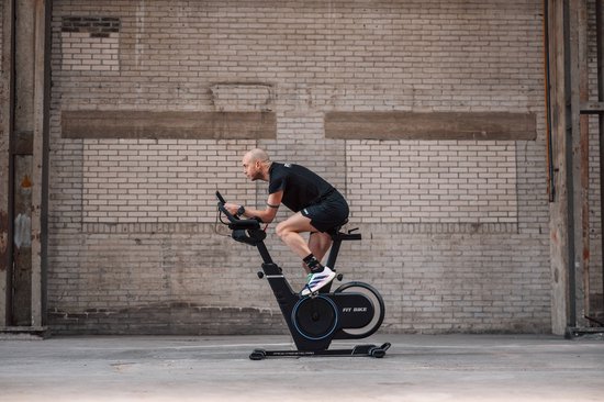 Man met zwart shirt en broek fietst op een zwarte Fit Bike Race Magnetic Pro spinfiets buiten.