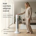 Een vrouw in een beige outfit raakt de witte JAP torenventilator aan in een woonkamer.