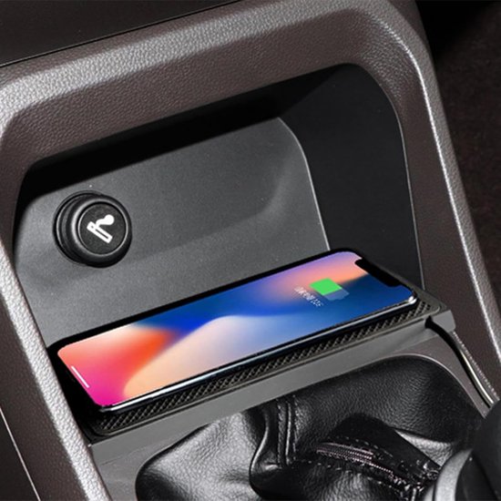 Een smartphone met een geopend scherm ligt op een zwart, gestructureerd oplaadstation in een auto-interieur.