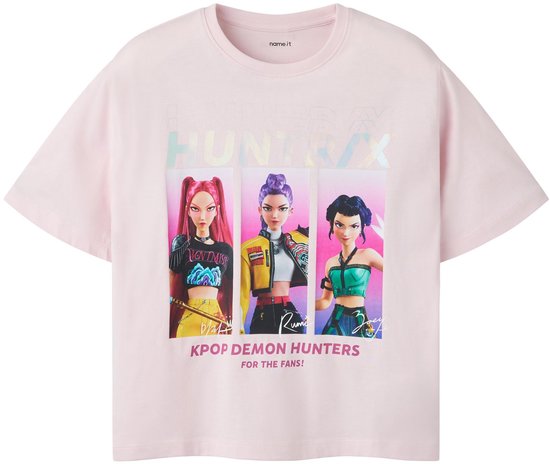 T-shirt rose pâle avec le texte « HUNTRX » et un imprimé de trois filles « KPOP DEMON HUNTERS » aux cheveux violets, roses et noirs.
