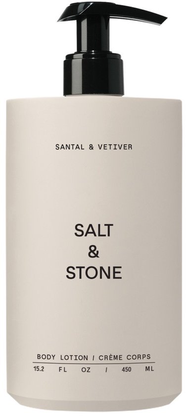 Crèmekleurige fles met zwarte pompdispenser voor bodylotion met 'SALT & STONE' en 'SANTAL & VETIVER' opdruk.