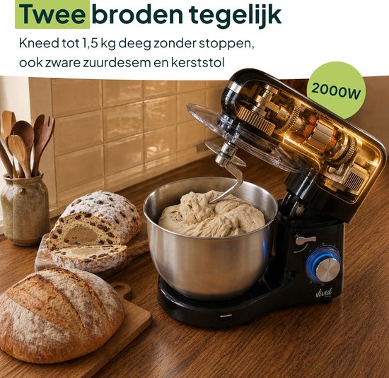 Zwarte keukenmixer met metalen kom vol deeg, naast twee broden en met zicht op interne tandwielen.