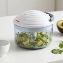 Witte hakker van Metaltex met een transparante container gevuld met gehakte avocado en rode ui, op een aanrecht. Een halve avocado ligt ernaast.
