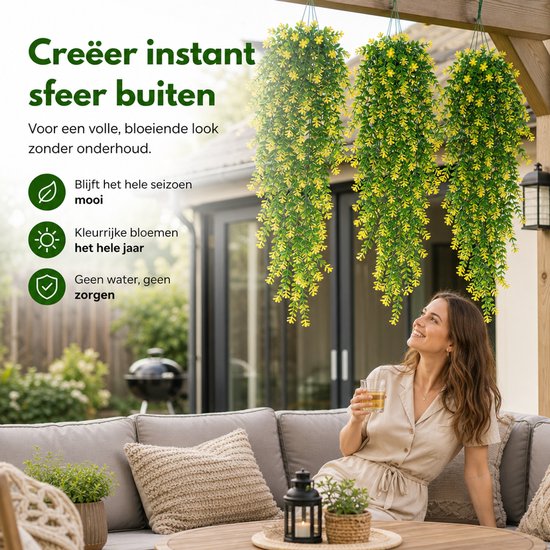 Een vrouw met een drankje, kijkt naar drie hangende kunstplanten met groene bladeren en gele bloemen op een terras.