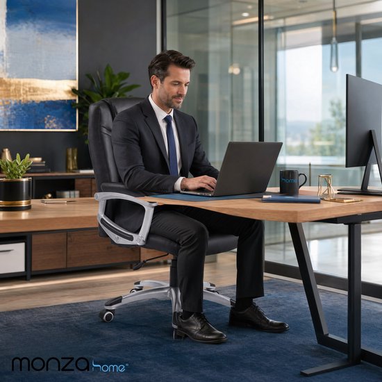 Man in zwart pak werkt op laptop in een modern kantoor, zittend in een zwarte bureaustoel.