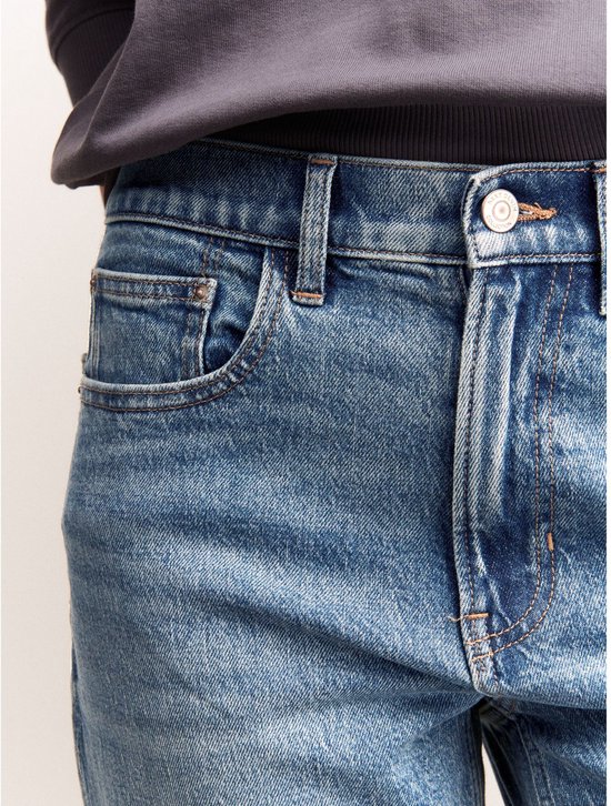 Close-up van de tailleband van een spijkerbroek met hoge taille, met zakken en een knoopsluiting.