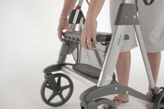 Handen van een vrouw vouwen een grijze rollator met een stoffen mandje op.