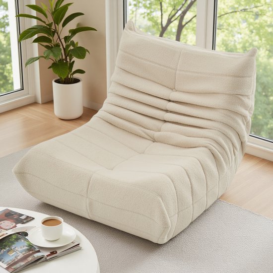 Beige pluche relaxfauteuil in een lichte woonkamer bij een raam.