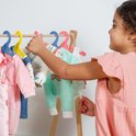 Een meisje kiest een mintgroene poppenjurk met pinguïns en regenboog uit, hangend aan een gele hanger.