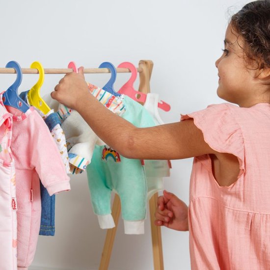 Een meisje kiest een mintgroene poppenjurk met pinguïns en regenboog uit, hangend aan een gele hanger.
