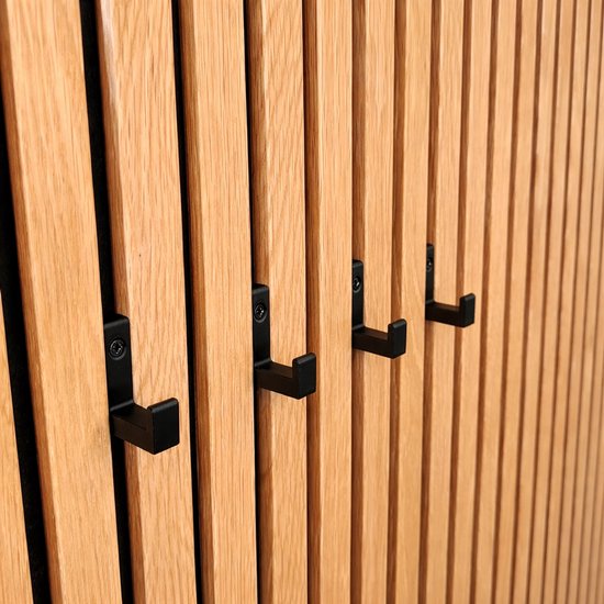 Quatre porte-manteaux Vleugel noirs fixés sur un mur à lamelles en bois.