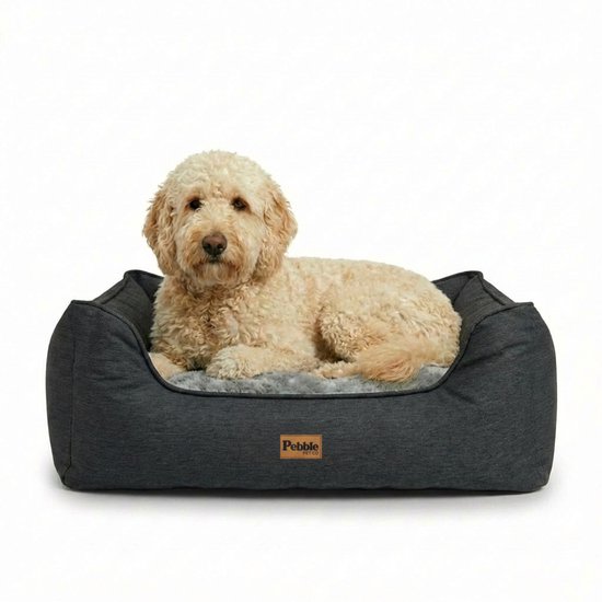 Un chien golden doodle est allongé dans un panier pour chien gris avec une doublure grise moelleuse.