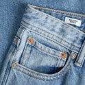 Detail van lichtblauwe jeans: tailleband, knoop en zak met klinknagels. Label 'RELAXED CHRIS'.