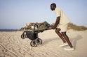 Man duwt kinderwagen met kind op een zandstrand bij de zee