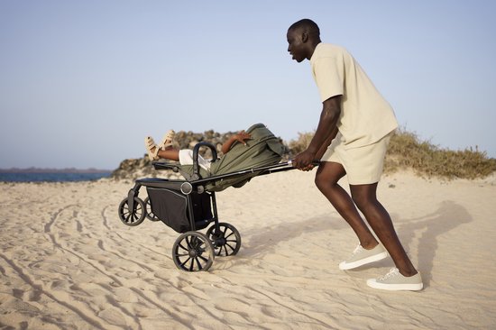 Man duwt kinderwagen met kind op een zandstrand bij de zee