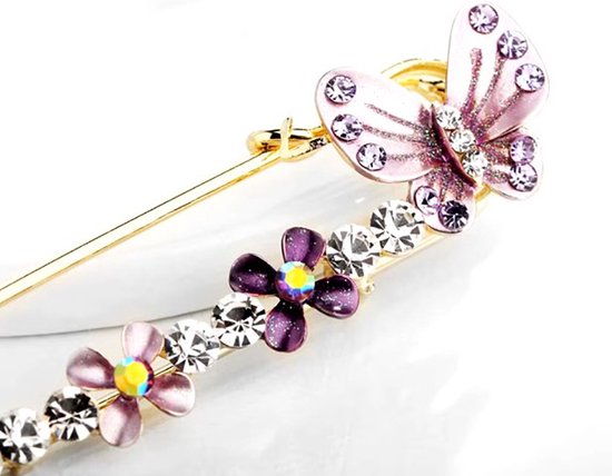 Close-up van gouden veiligheidsspeld met vlinder en bloemetjes, paarse en heldere strass steentjes.