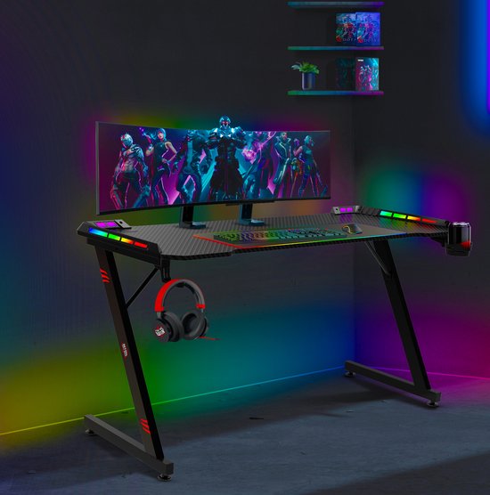 Zwart gaming bureau met z-vormige poten, RGB LED verlichting, gedecoreerd met een gebogen monitor, toetsenbord en koptelefoon.