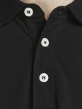 Sluiting van een zwart poloshirt met witte knopen met logo.