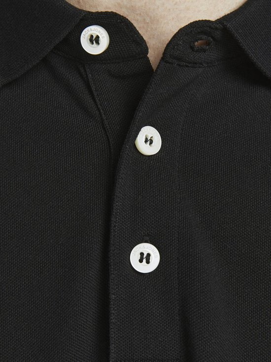 Sluiting van een zwart poloshirt met witte knopen met logo.