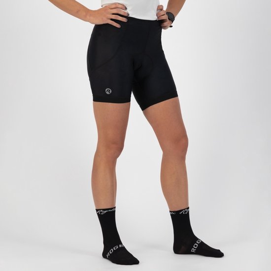 Femme, mains sur les hanches, debout en débardeur blanc et cuissard noir, avec des chaussettes noires à logo.