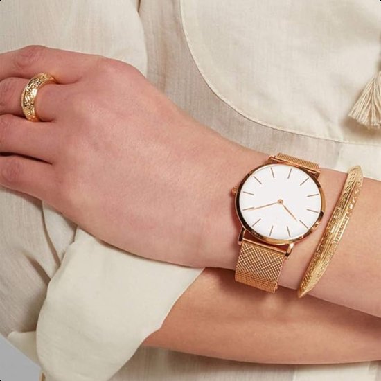 Dameshorloge met witte wijzerplaat en zilverkleurige mesh band. Gedragen op een pols met een gouden ring en armband.
