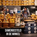 Twee medewerkers in een winkel vol kazen, een geit en de tekst 'SAMENGESTELD IN DE WINKEL'.