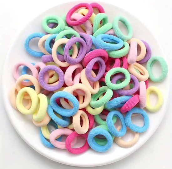 Een stapel zachte, pastelkleurige haar elastiekjes in verschillende kleuren, waaronder roze, paars, geel, blauw en groen, op een witte schaal.