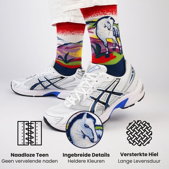Een paar rode sokken met de print van een wit paard en kleurrijke achtergrond, gedragen met witte sneakers en witte shorts. Vergroot detail van het paardenhoofd.
