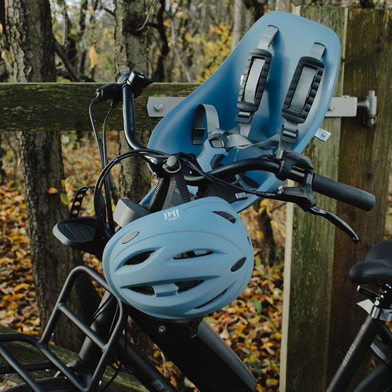 Lichtblauwe fietshelm met ventilatieopeningen, naast een kinderzitje op een fiets.