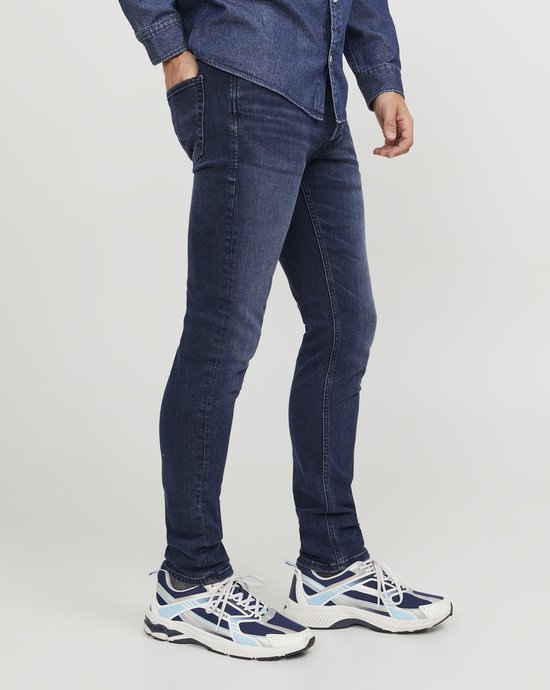 Blauwe skinny jeans gedragen door een man met spierwitte sneakers en een spierwitte denim blouse.