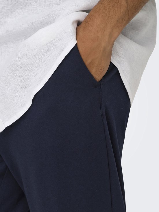 Detail van de zak van een donkere broek met de hand erin.