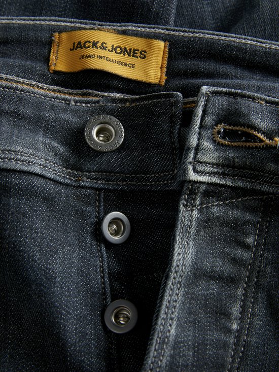 Sluiting detail van een donkere jeans met gele merklabel.