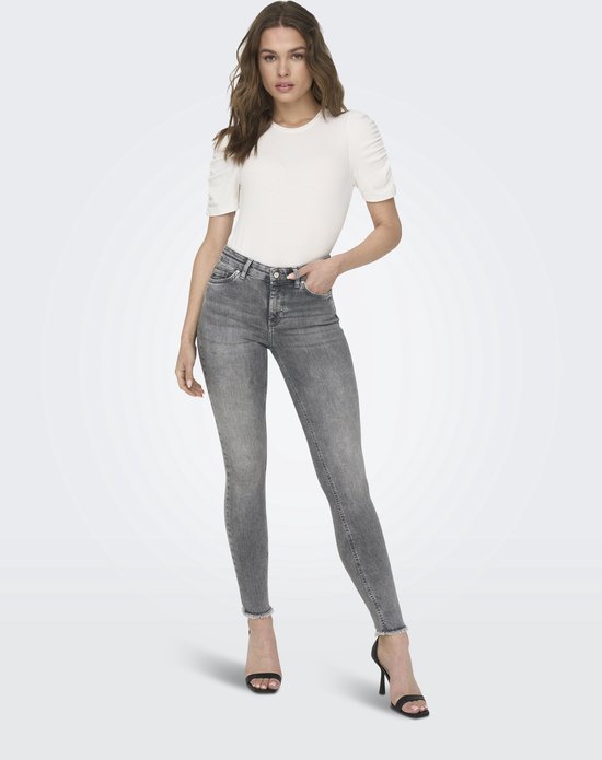 Model draagt grijze skinny jeans met middelhoge taille, rafelige zoom en witte top.