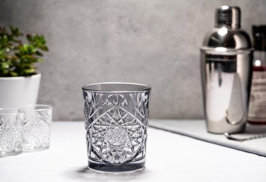 Transparant glas met geometrisch patroon, naast cocktailshaker en plant.