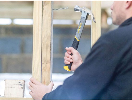 Man met een grijze en zwarte klauwhamer met gele accenten in een houten constructie.