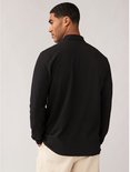 Man kijkt weg, draagt een zwart poloshirt met lange mouwen, van achteren gezien.