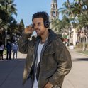 Man met kroeshaar en parelketting past zijn zwarte JLab open-ear koptelefoon aan.