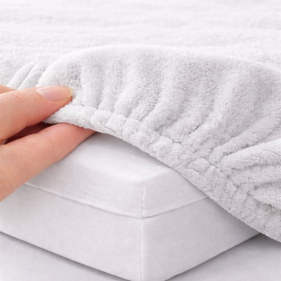 Een hand toont de zachte, geribbelde stof van een lichtgrijs badstof hoeslaken dat over een matras wordt getrokken.