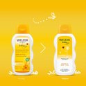 Weleda verzorgende babyolie in witte fles met gele dop, met bloemen en lieveheersbeestje.