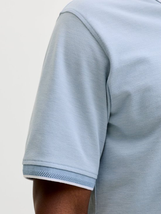 Close-up van de mouw van een lichtblauw poloshirt met witte rand.