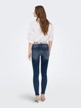 Vrouw met lang bruin haar in een witte blouse en donkerblauwe skinny jeans met rafels aan de onderkant.
